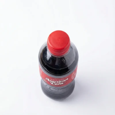 Bouteille en plastique d'AMERICAN COLA 35 cl en vue de dessus, avec son bouchon rouge vif et son étiquette rouge sur fond blanc.