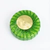 Vue de dessus du BLOC DESODORISANT ASSORTIS, rond et vert, dans son emballage plastique plissé avec une étiquette dorée.