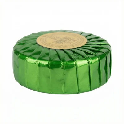 Vue de latérale d'un bloc désodorisant assortis rond, dans son emballage plissé d'un vert métallique et brillant.