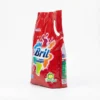 Vue latérale du sachet rouge du DETERGENT BRIL 900G, avec poignée et design d'éclaboussures multicolores sur fond blanc.