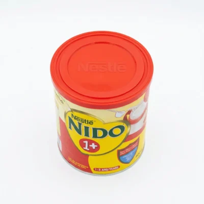 Vue de dessus d'une boîte cylindrique de lait en poudre Nestlé NIDO 1+ avec son couvercle rouge et son étiquette jaune.