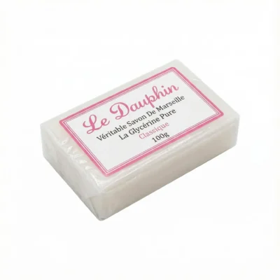 Vue de dessus du SAVON LE DAUPHIN CLASSIQUE 100G, un pain blanc rectangulaire sous plastique transparent avec étiquette rose.