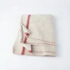 Vue de dessus d'une serpillière pliée en coton écru à rayures rouges, au tissage épais et texturé sur fond blanc.